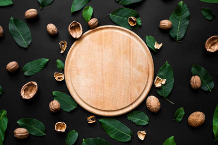nutshell and fresh green leafs  scattered on a black background. Wooden cutting board in the centreの写真素材