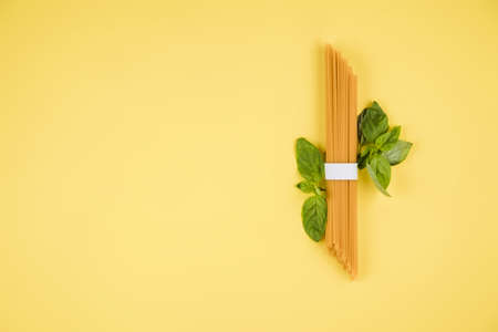 Spaghetti, basil on a yellow background. Top view. Copy space for text.の写真素材