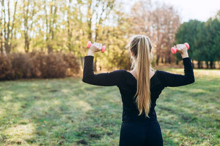 Fitness in the park, girl holding dumbbells, back view.の写真素材