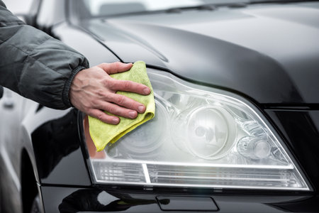 A man cleaning car's frontal headlights with microfiber cloth, car detailing  concept.の写真素材