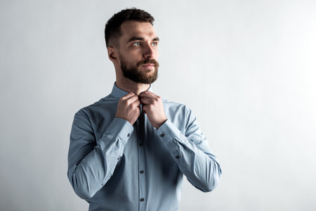 Studio portrait of seriously guy fastens a button on a shirt.