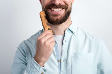 Closeup  crop portrait of bearded man combing his beard. Closeup smile. - Imageの写真素材