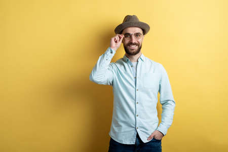 Man wearing in casual clothes, glasses and hat standing and cheeerful smiling touches himself glasses against an yellow background.の写真素材