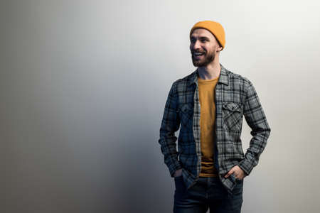 laughing guy with a beard dressed in  checkered shirt and yellow hat holds his hands in the pockets. - Empty copyspaceの写真素材