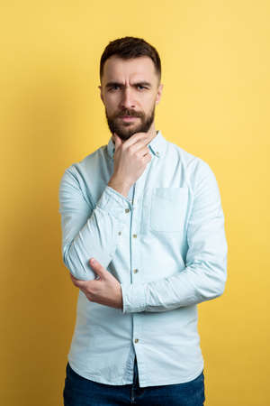 Studio male waist portrait. Man toushes himself chin and frown seriously looking at the camera folded his hands.の写真素材