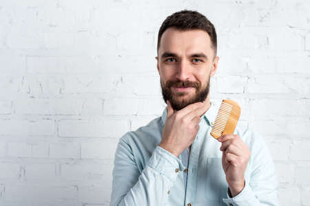 Closeup portrait of happy  bearded man holding a comb touches  his  beard and looking at the camera.の写真素材