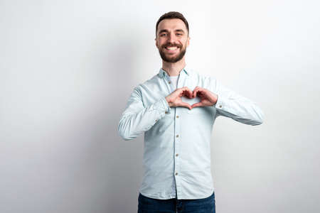 Studio shot portrait of happy bearded man showing a gesture heart from his arms. - Imageの写真素材