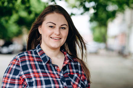 Smiling beautiful woman looking straight into the camera on the street under a green treeの写真素材