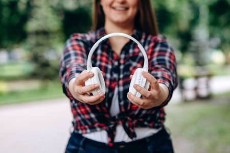 Woman plus size in colorful shirt holding wireless headphones, outdoorsの写真素材