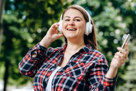 Charming, modern woman in white, wireless headphones having fun outdoorsの写真素材