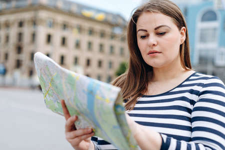 Young beautiful tourist girl stands on the square, carefully studying the tourist mapの写真素材