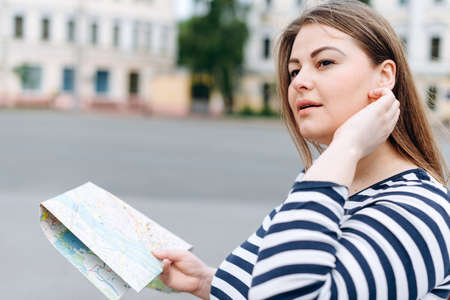 Travel girl visiting city with map in her hands and looking around. Happy cheerful female tourist exploring new city looking to the side.の写真素材