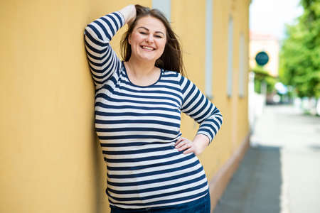 Smiling cheerful woman plus size posing outdoors on orange wall backgroundの写真素材