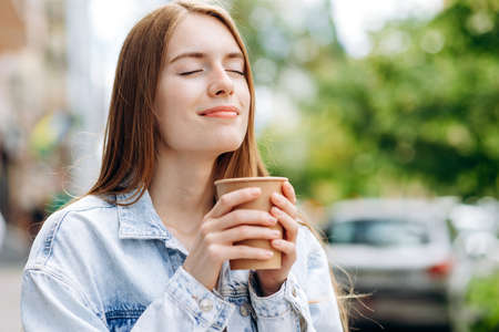 Cute young woman closing her eyes enjoying a sip of coffee outdoorsの写真素材