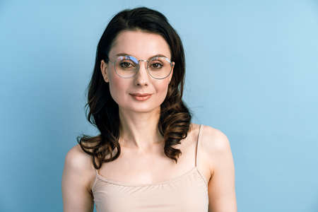 Close up beautiful brunette in glasses posing on a blue background. Isolated on blue background, copy space.の写真素材