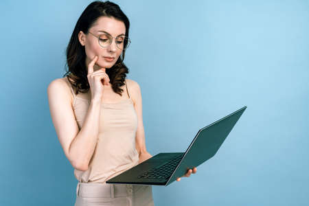Serious girl is working on a laptop, thinking and analyzing something. Girl isolated on a blue background.の写真素材