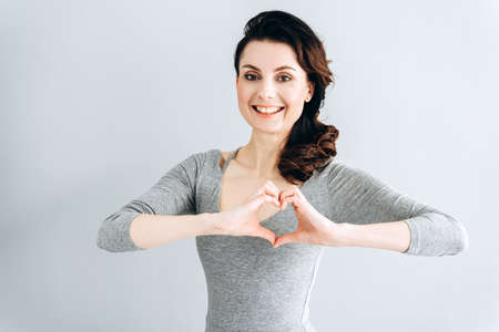 Close up photo of a beautiful amazing lady shows heart with fingers. Beautiful woman isolated on gray background, copy space.の写真素材