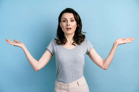 Confused girl with open arms doubts on a blue background. Isolated on gray background, copy space, place for advertising.の写真素材
