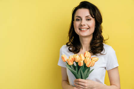Young woman with flowers on a yellow background. Smiling, cute woman isolated on blank wall background, copy space.の写真素材