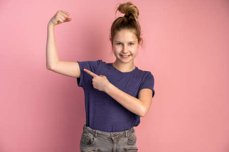 Beautiful teenage girl shows her muscles on a pink background. Cute teenager isolated on blank wall.の写真素材