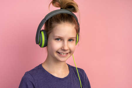 Attractive teenage girl on a pink background in headphones. Beautiful little girl smiling on a blank wall background.の写真素材