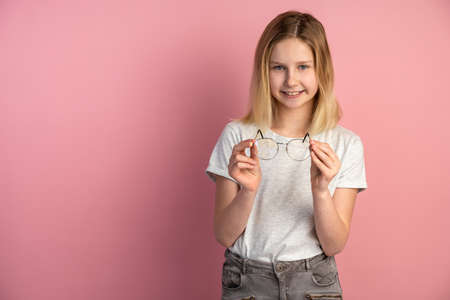 Charming, pretty girl with glasses in her hands posing on the background of an empty wall. Girl standing on a pink background in the studioの写真素材