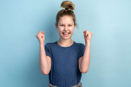 Beautiful teen girl making a triumphant gesture on a blue background. Emotional girl gesturing in isolation on a blank wall.の写真素材