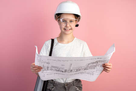 Cute little girl in a construction helmet on a pink background. Teenager holding a drawing in his...