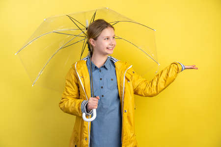 Cheerful child girl with umbrella and yellow rain coat on yellow background. Copy space for textの写真素材