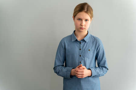 Sad little girl in a blue shirt on a white background. Isolated on blank wall, copy space.の写真素材