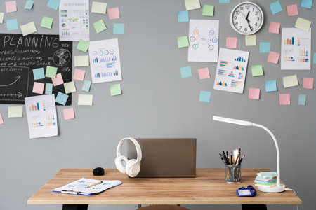 Workplace. On the desktop laptop, headphones, notebook for planning. Multicolored stickers, graphs...