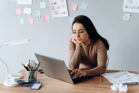 Girl working on laptop. Business girl with glasses works carefully sitting at the desk.の写真素材