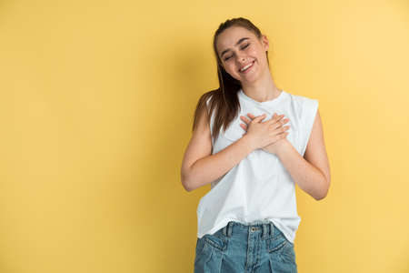 Portrait of positive girl putting hands on chest feel good wearing casual lifestyle outfit isolated over yellow background. Beautiful girl isolated on a blank wall.の写真素材