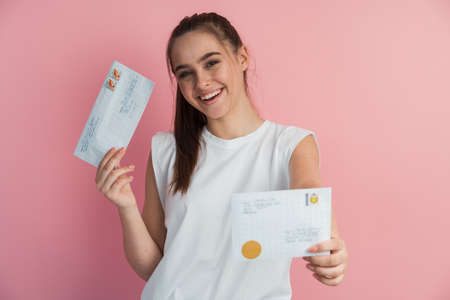 Close-up view of a cute, sincere, young girl with mail envelopes on a pink background. Beautiful lady on a blank wall background.の写真素材