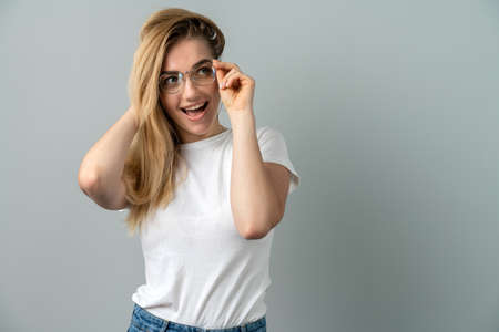 Young blonde woman in glasses on a gray background. Young girl posing on a background of a gray wallの写真素材