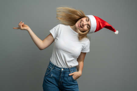 Girl having fun on a background of a gray wall. Funny young woman in santa hat isolated on gray background.の写真素材