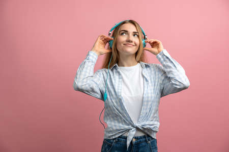 Dreamy girl on a pink background in headphones listens to music. Young girl posing isolated on a...