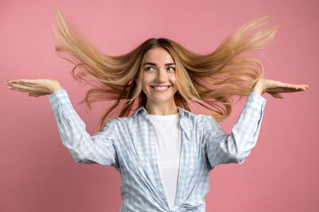 Young, beautiful woman playing with her hair. Against the background of a pink wall, hair flies in the air.の写真素材