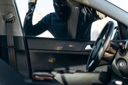View from the car at the man dressed in black with a balaclava on his head preparing breaking with...
