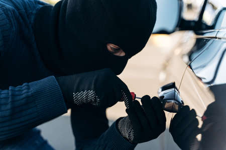 Close up view of the dangerous man dressed in black with a balaclava on his head picks the lock with a pick while stealing. Car thief, car theft conceptの写真素材