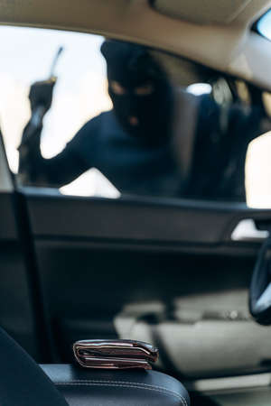 Vertical view from the car at the man dressed in black with a balaclava on his head preparing breaking with crowbar the glass of car before the stealing. Car thief, car theft conceptの写真素材