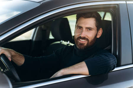 Happy caucasian man sitting and looking at the window while having long road by the car. Busy people...
