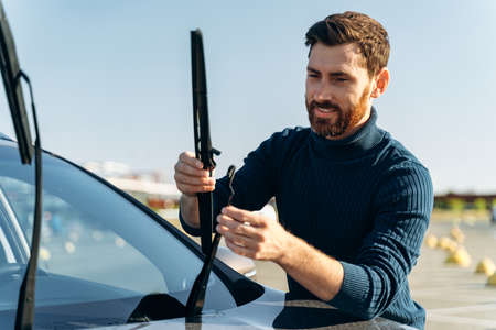 Male auto owner checking windshield wiper at the street. Man is changing windscreen wipers on a car. Automobile repair conceptの写真素材