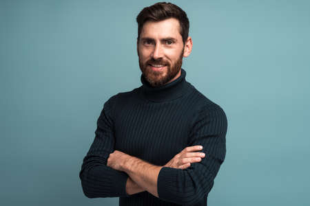 Portrait of happy satisfied handsome young man standing with crossed arms and looking at camera with toothy smile. Indoor studio shot on blue background copy spaceの写真素材
