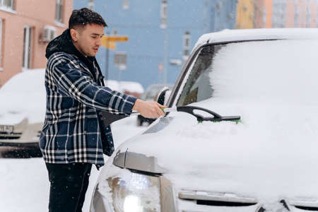 Attractive man cleaning snow off his car during the snowy winter day. Transportation, vehicle and car care concept during winterの写真素材