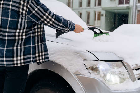 Cropped view of the caucasian man cleaning snow off his car during winter snowfall. Transportation and seasons conceptの写真素材