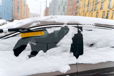 Cropped view of the parked car covered with snow after snowfall in winter. Unrecognizable person using special brush for cleaning car from the snowの写真素材