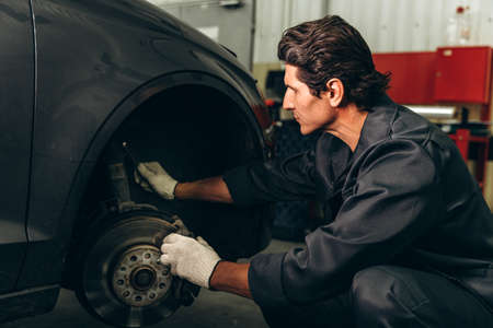 Serious mechanic wearing gloves preparing to placing a wheel into a car. Car checkup and car service concept. Stock photoの写真素材