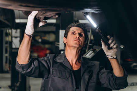 Car service, repair and people concept. Waist up portrait view of the auto mechanic man with lamp working at the workshopの写真素材