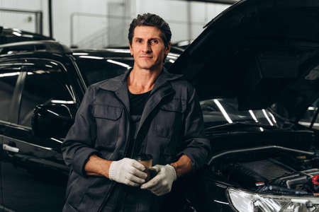 Waist up portrait view of the calm confident senior auto mechanic wearing gloves standing near the...